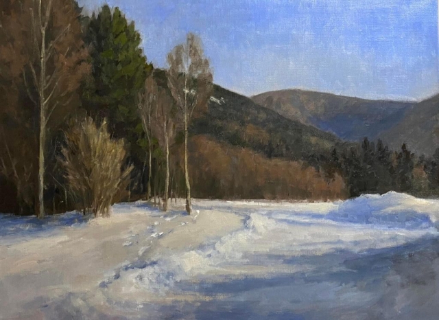 Footprints in the snow lead to a group of trees. Snowy scene with hills in the background.